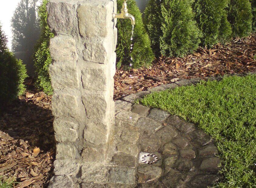 Stylowy kamienny kran ogrodowy w zieleni.